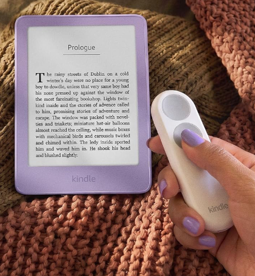 A purple Kindle showing a book's prologue, beside a hand holding a white two-button Kindle Click remote.